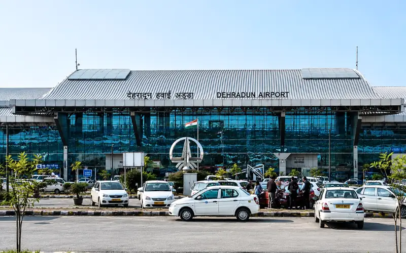 Dehradun airport taxi service at Jolly Grant Airport terminal with cars and passenger pickup area
